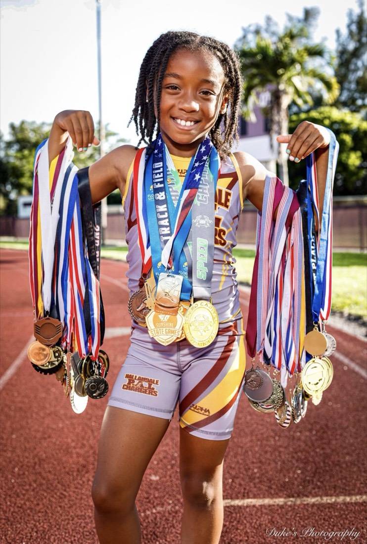Storm Randolph on a running track, smiling and holding up dozens of track and field medals